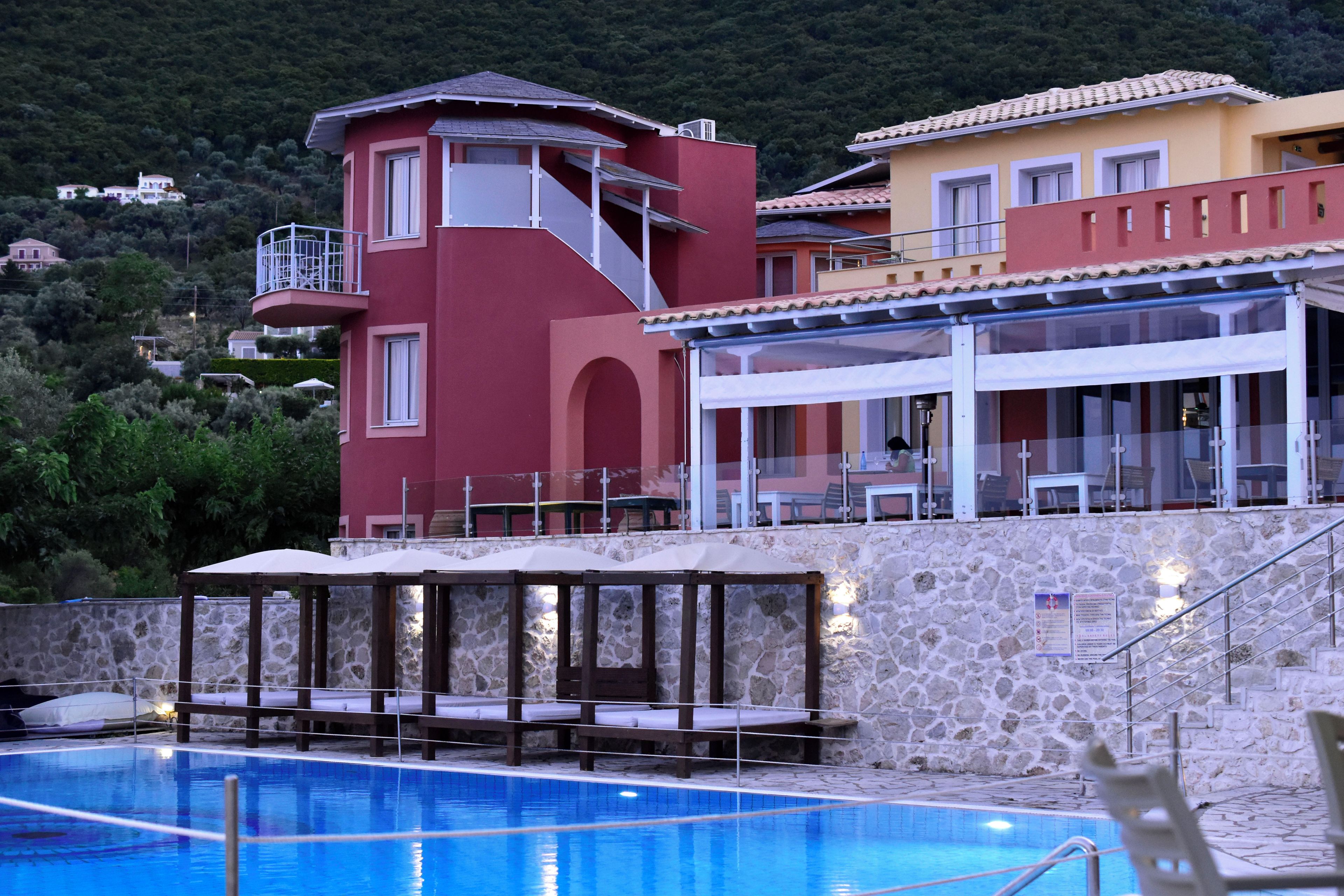 A pool area with a stone wall, a red building, and a yellow building with a balcony.