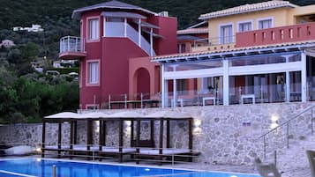 A pool area with a stone wall, a red building, and a yellow building with a balcony.