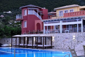 A pool area with a stone wall, a red building, and a yellow building with a balcony. - Red Tower (Lefkada)