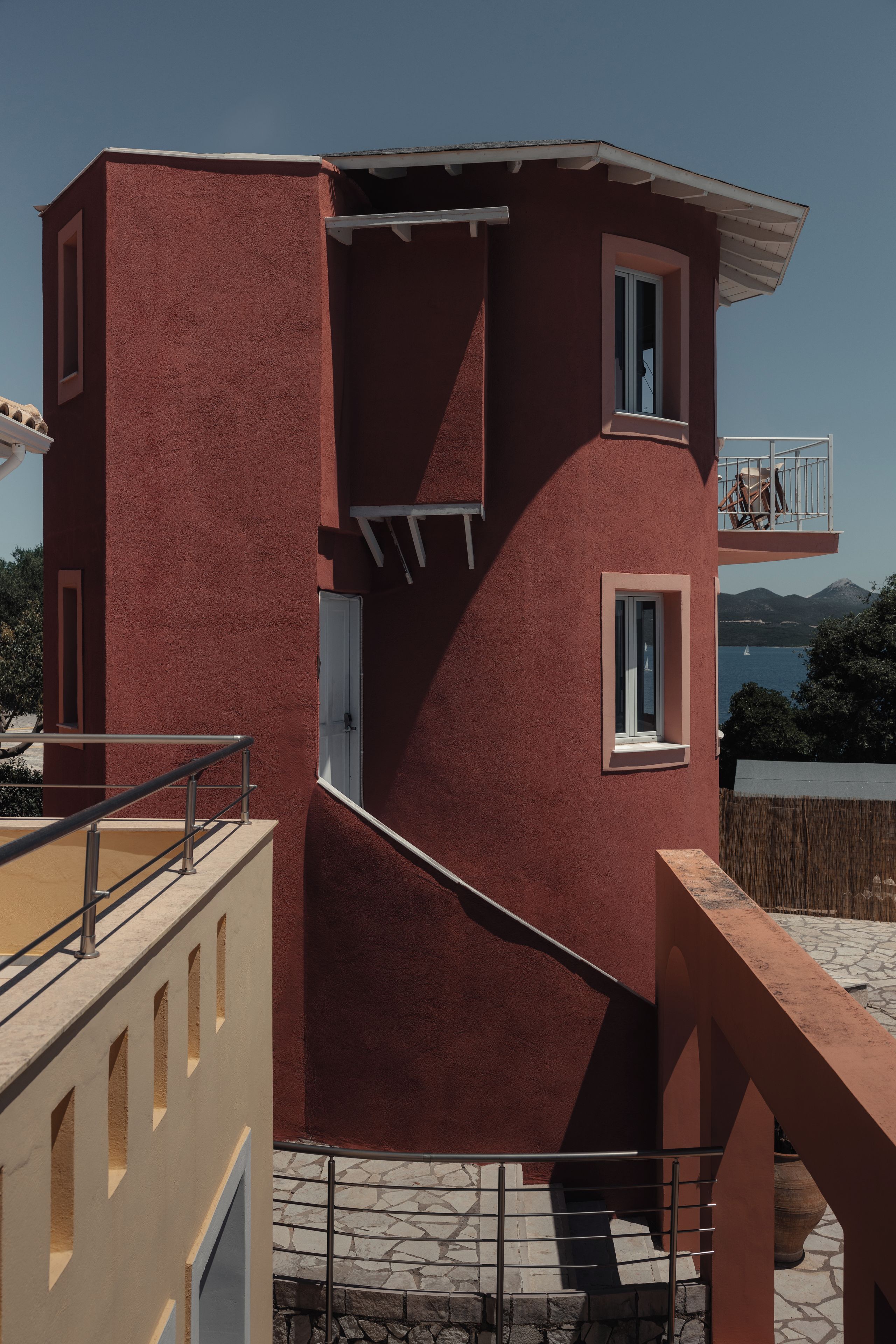 A red building with a balcony, a staircase, and a view of the sea.