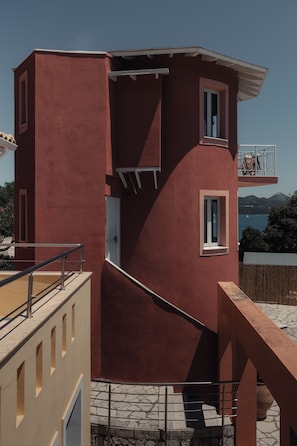 Een rood gebouw met een balkon, een trap en uitzicht op zee.