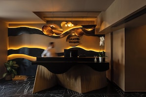 A reception desk with a modern design, featuring a curved wooden base and a black countertop. There is a sign above the desk that reads "SANTO MANGOPPA." - Santo Mangata Boutique Hotel & Spa (Santorini)