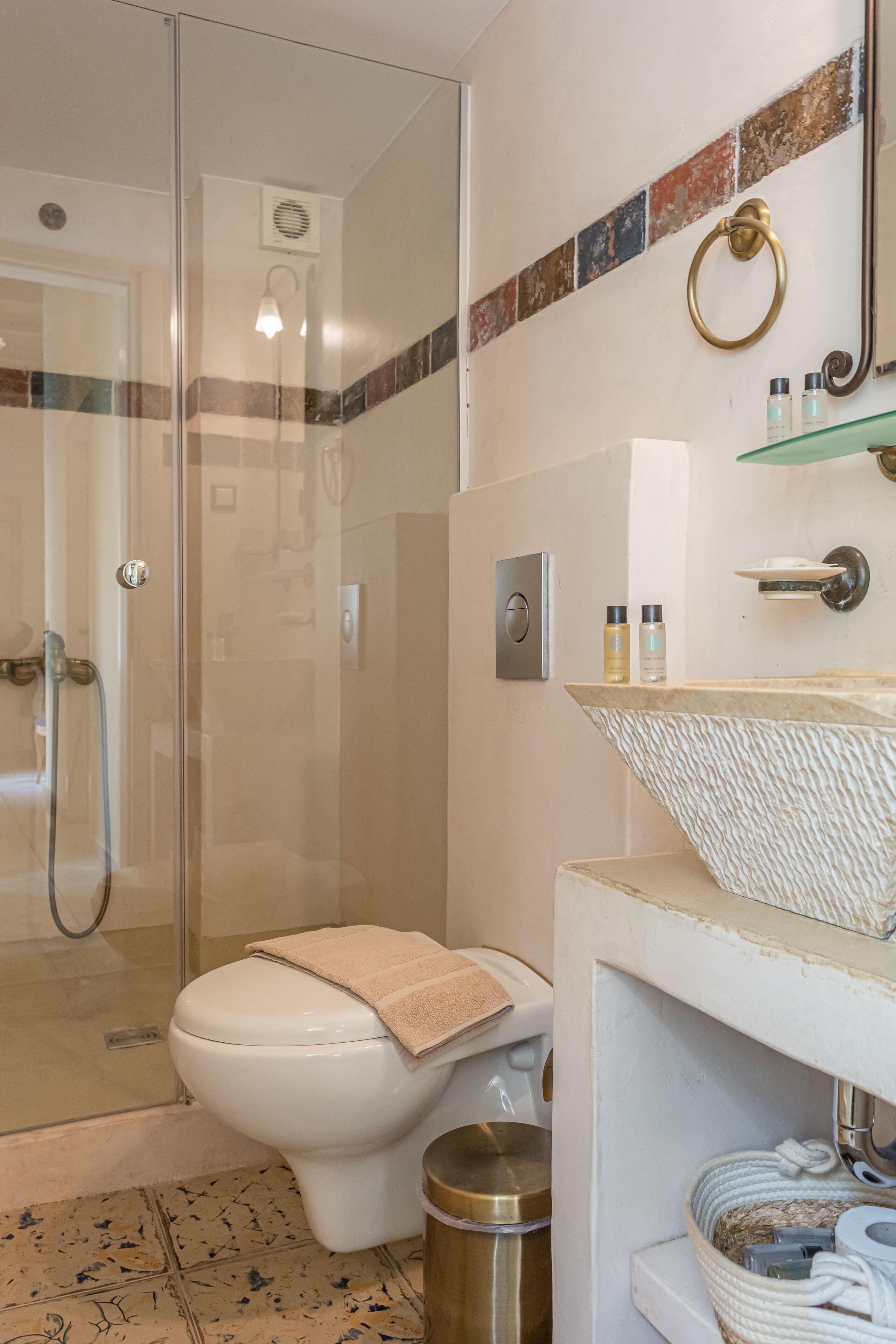 Un baño con ducha envuelta en vidrio, inodoro con toalla y lavamanos con artículos de aseo.