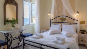 A neatly arranged bedroom with a bed, bedside tables, a mirror, and a view of the sea through a window. - Pandora Suites (Chania)