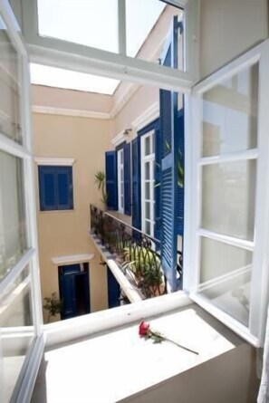 A view from a window with blue shutters, a balcony with plants, and a rose on the windowsill. - Pandora Suites (Chania)
