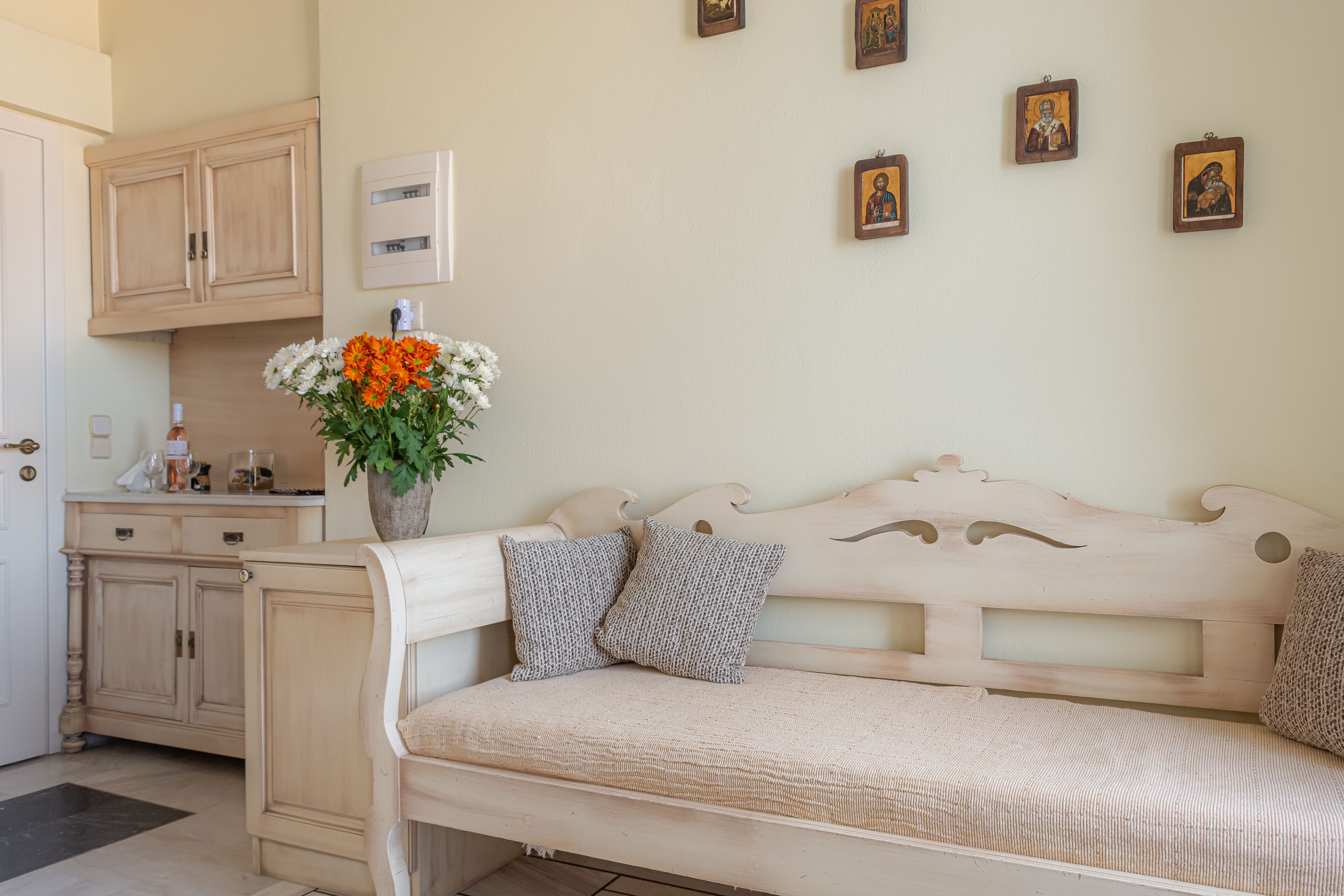 Una habitación acogedora con un banco de madera, un florero con flores e iconos religiosos en la pared.