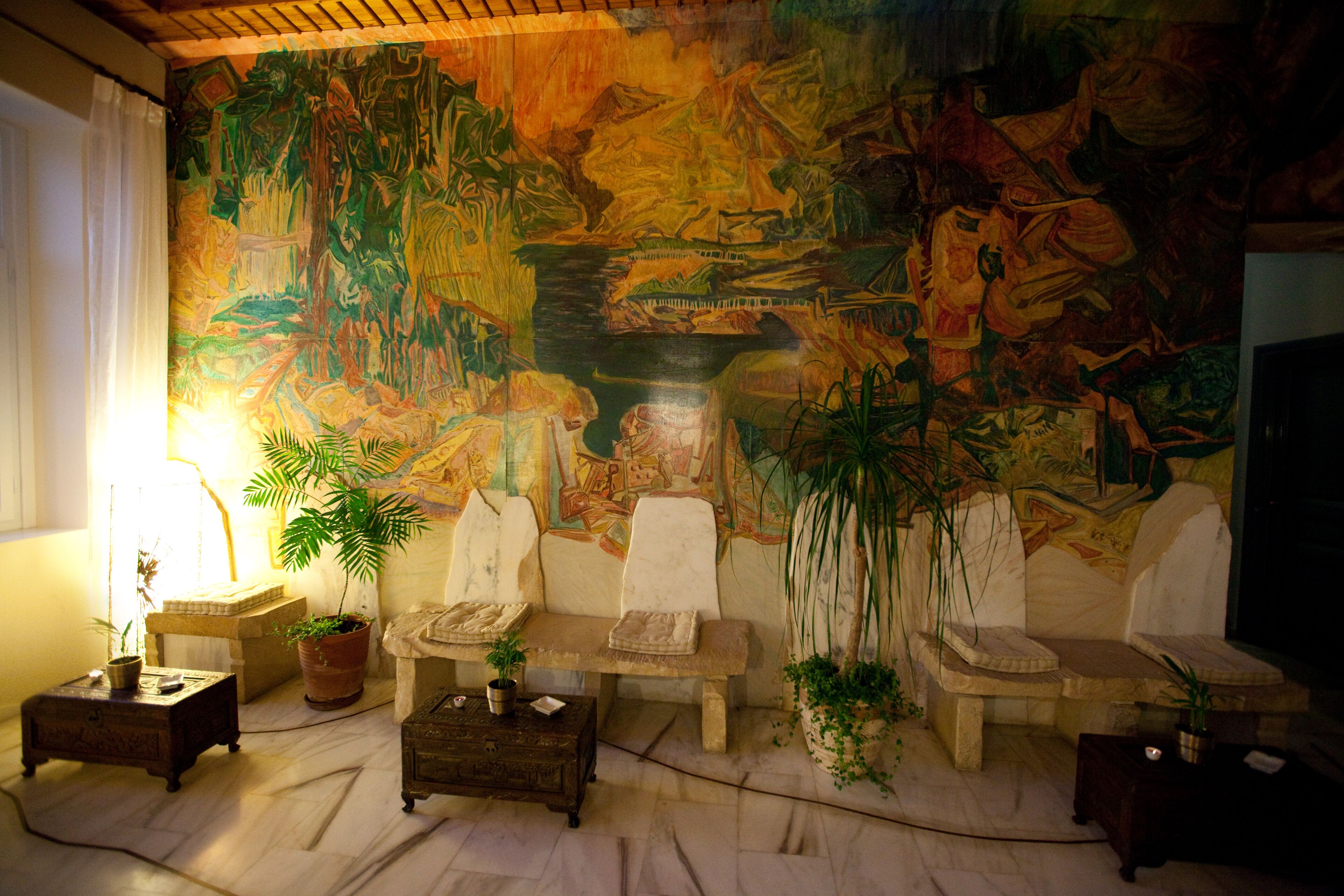 A room with a large mural, a sofa, a coffee table, and potted plants.