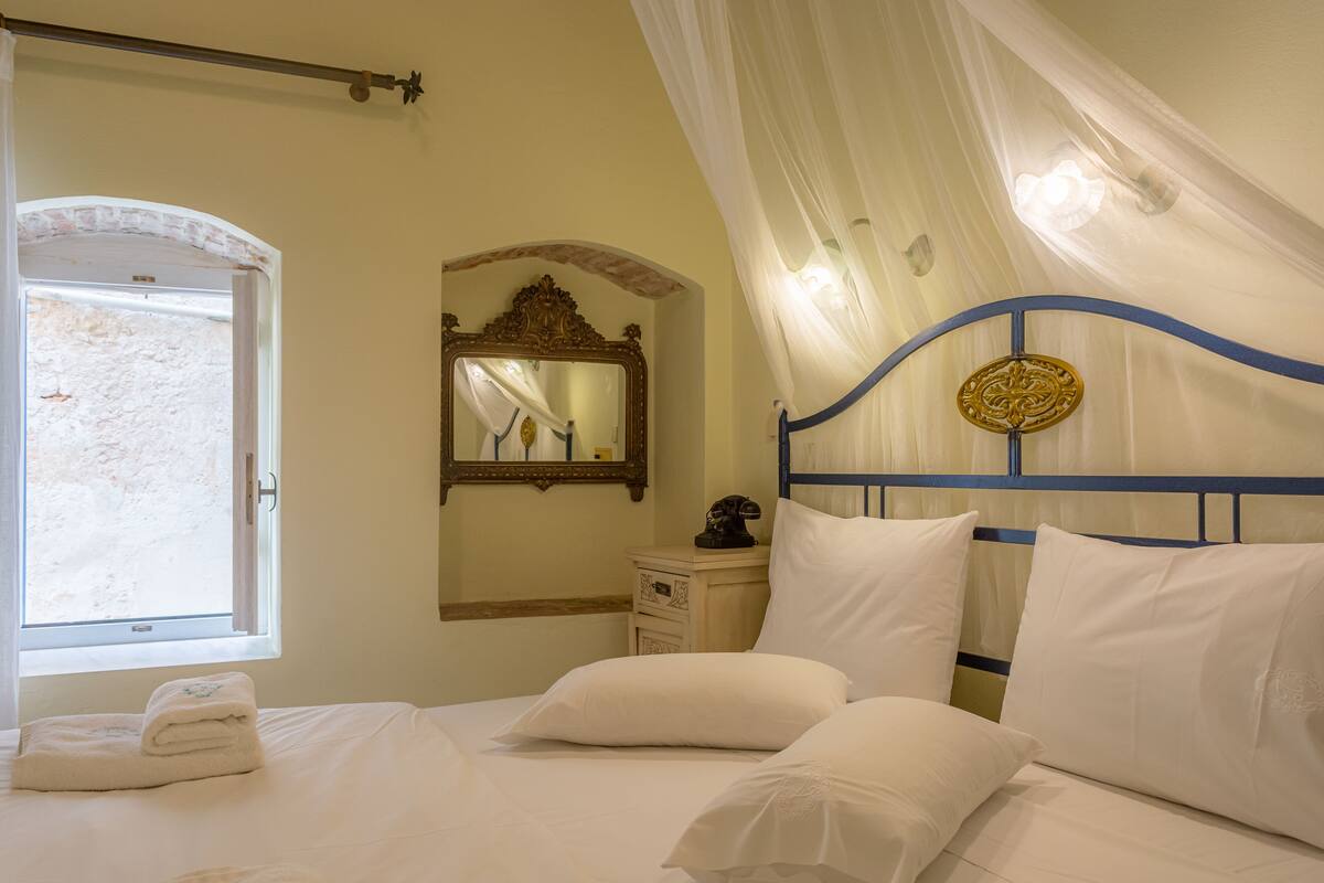 A bedroom with a bed, a nightstand, a mirror, and a window with curtains.