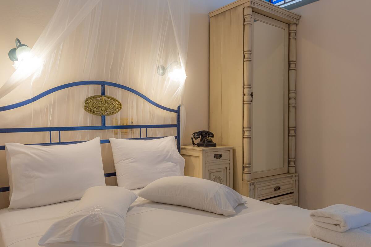 A neatly made bed with white linens and pillows, a bedside table with a telephone, and a tall wardrobe with a mirror.