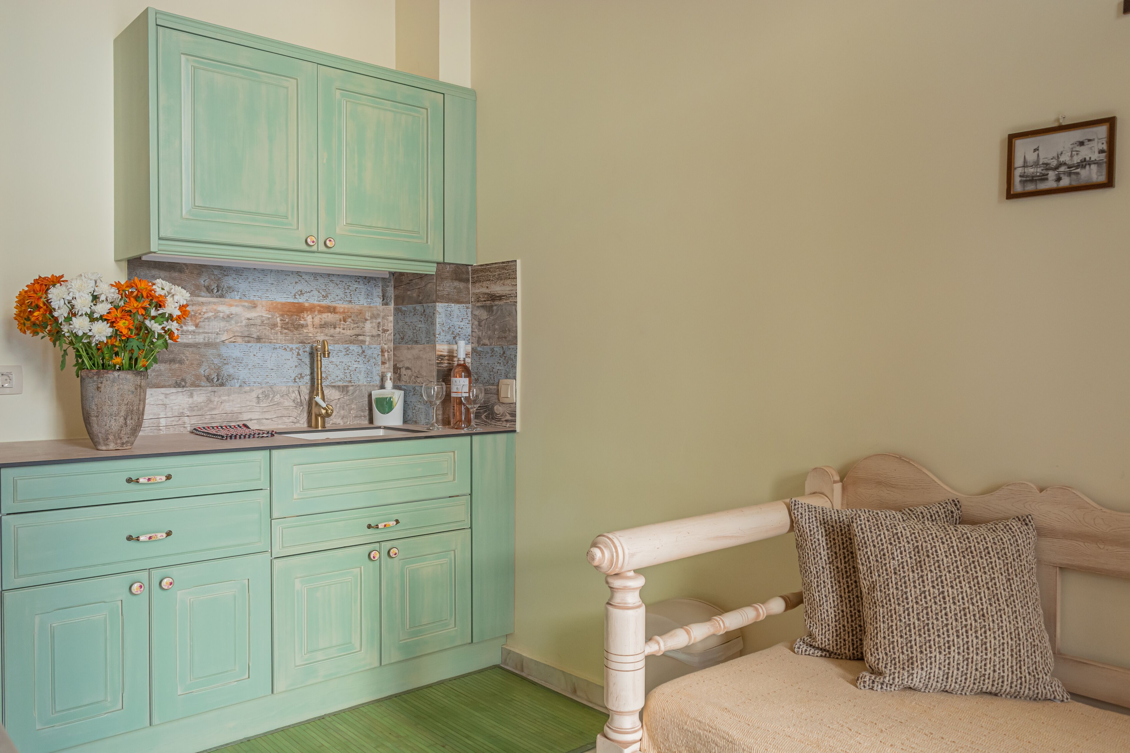 Une pièce avec des meubles de rangement de couleur turquoise, un lit avec une literie beige et une petite table sur laquelle est posé un vase de fleurs.