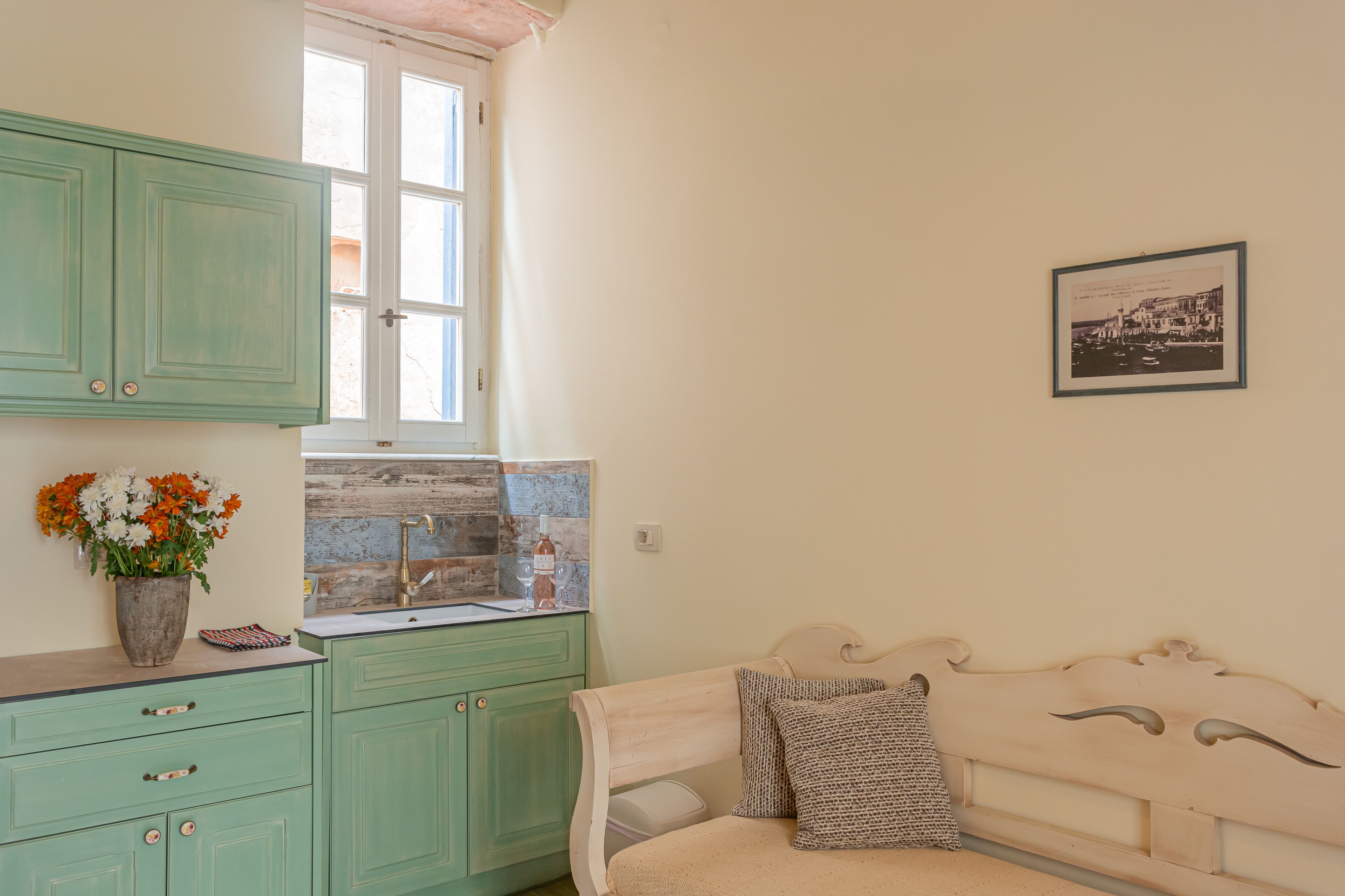A kitchen with green cabinets, a window, a sink, and a framed picture on the wall.