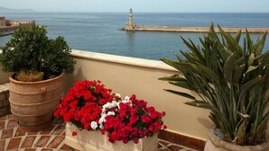 A terrace with potted plants and flowers overlooking a coastal view with a lighthouse. - Pandora Suites (Chania)