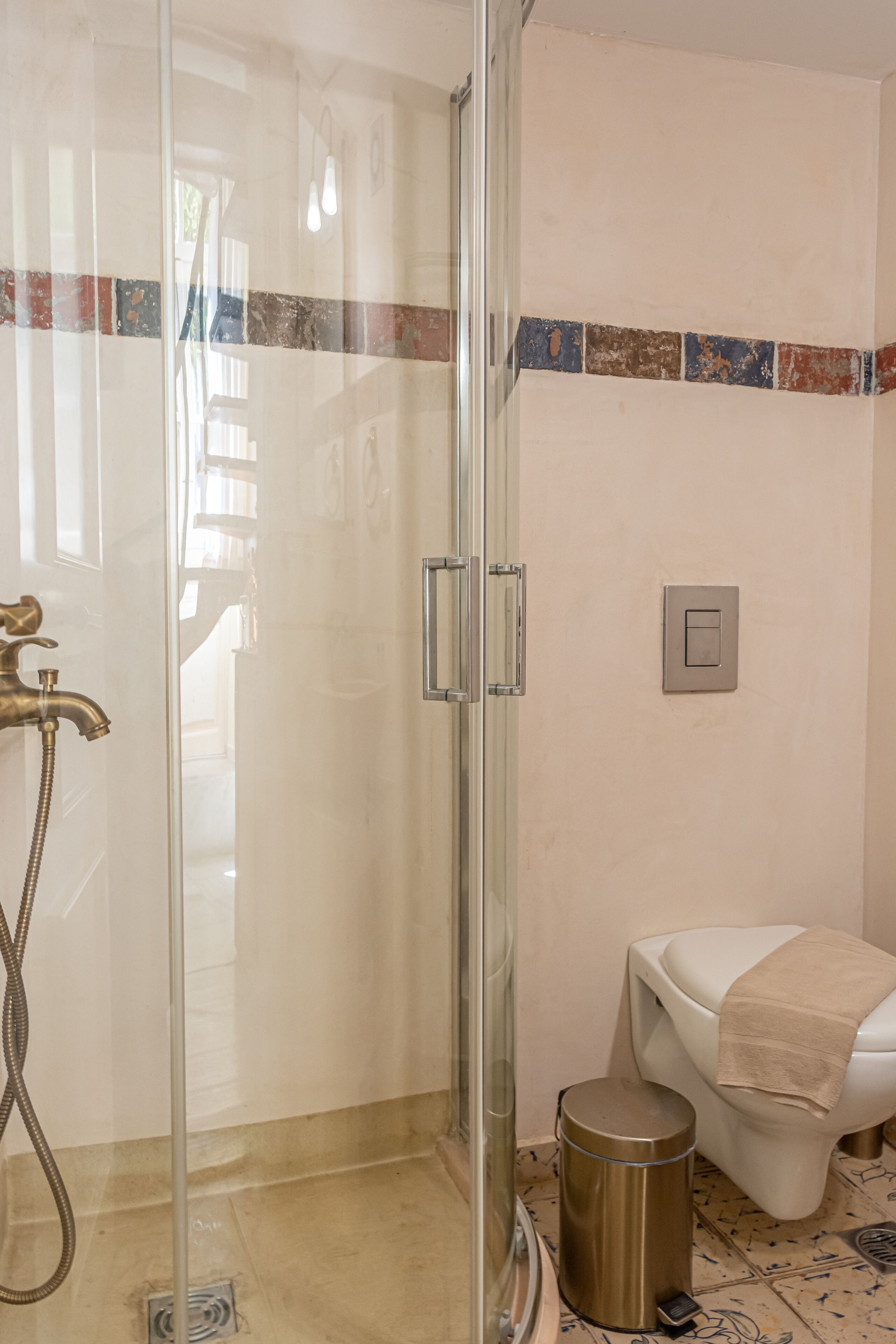 A bathroom with a glass shower enclosure, a toilet, and a trash can.