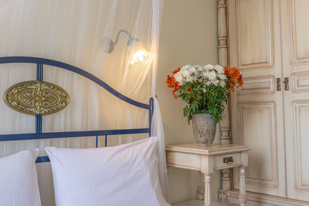 A neatly made bed with white linens, a bedside table with a vase of flowers, and a wardrobe with a light wood finish.