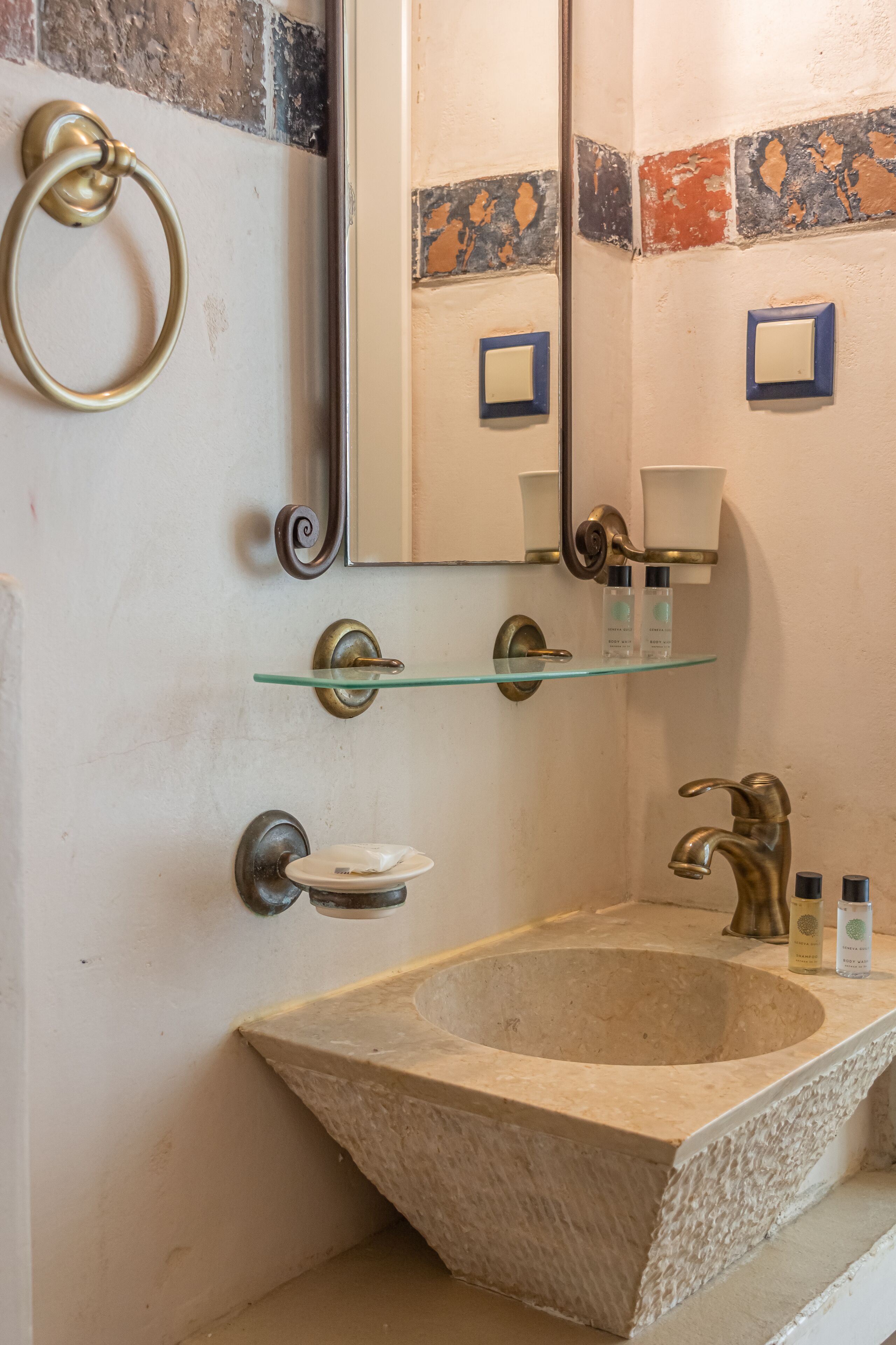 A bathroom with a stone sink, glass shelf, and a mirror.