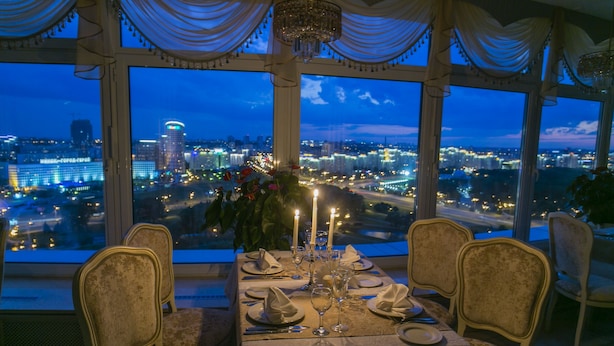 Mesa de comedor preparada para cuatro con vista a la ciudad, candelabros y cortinas drapeadas.
