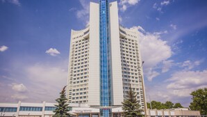 A tall hotel with a central glass tower, multiple floors, and a sign at the top. - Belarus Hotel (Minsk)