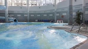 Una amplia piscina interior con tobogán, zonas de estar y vistas al piso superior.