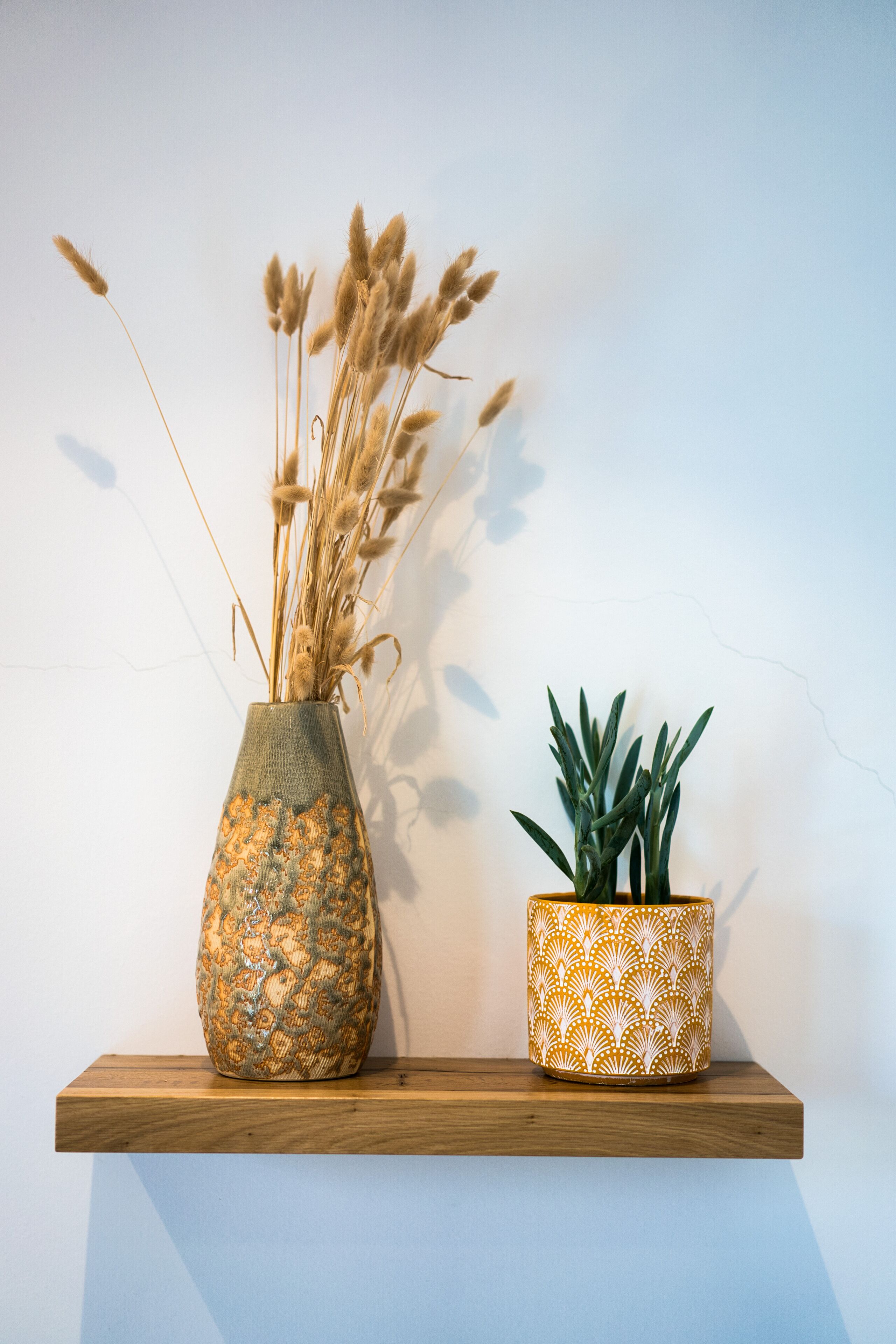 A wooden shelf with a vase of dried plants and a potted plant.