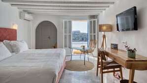 Un dormitorio con cama, escritorio, silla, televisión y vistas al exterior.