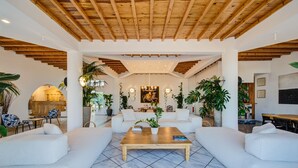 Amplia sala de estar con techo de madera, sofás blancos, una mesa de centro y plantas en macetas.