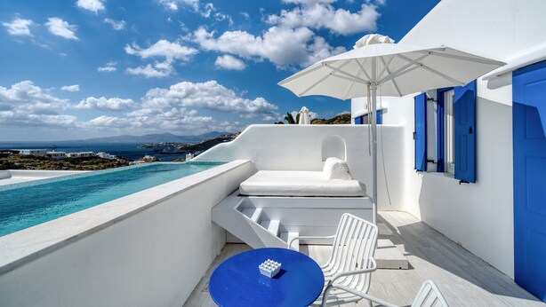 Una habitación en blanco y azul con una piscina, una silla blanca, una mesa azul y un paraguas blanco.