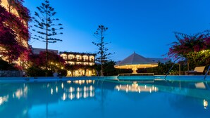 Une piscine dont la surface reflète les lumières, entourée de bâtiments et d’arbres.