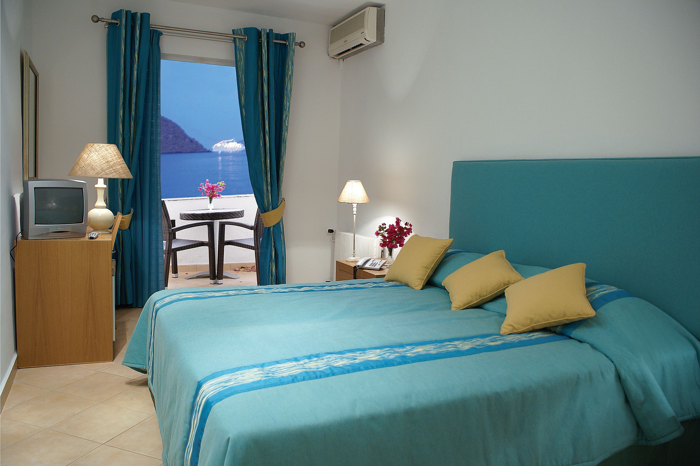 Habitación de hotel con una cama, un escritorio con computadora, una silla y vista al mar.