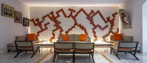 A living room with a sofa set, two armchairs, and a patterned wall decoration.