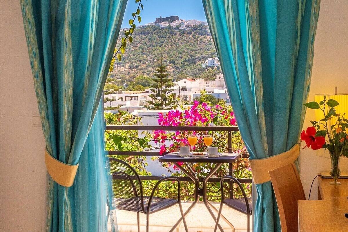 A balcony with a table and chairs, curtains, and a view of a hill with buildings.