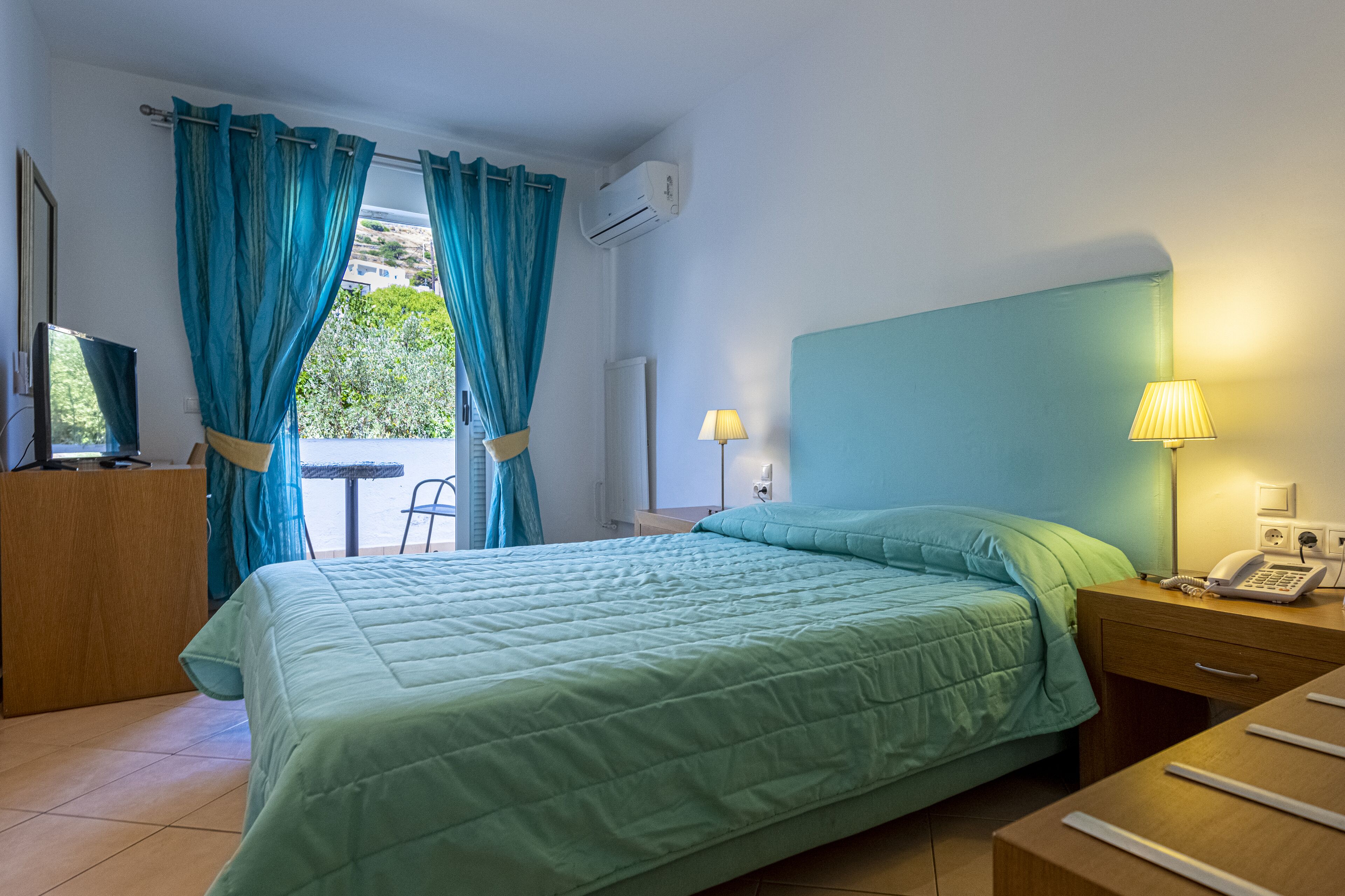 Una habitación de hotel con una cama, un escritorio, una silla, una lámpara y un equipo de aire acondicionado.