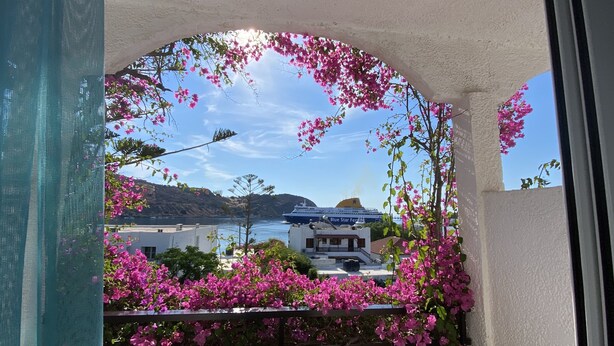 Un balcon orné de fleurs roses, d’où l’on peut admirer un navire de croisière appelé Blue Star Ferry.
