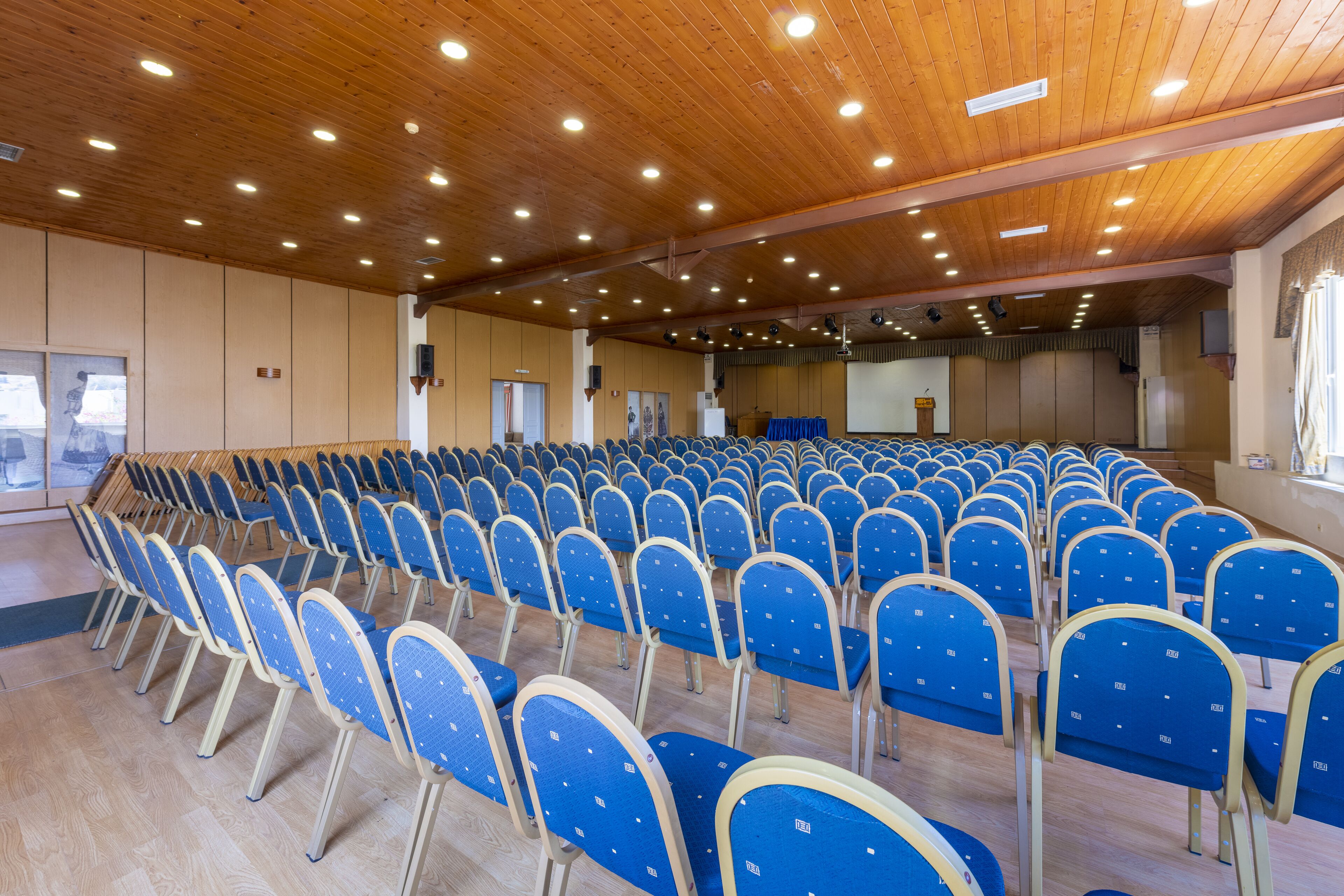 Une grande salle avec des rangées de chaises bleues et une scène.