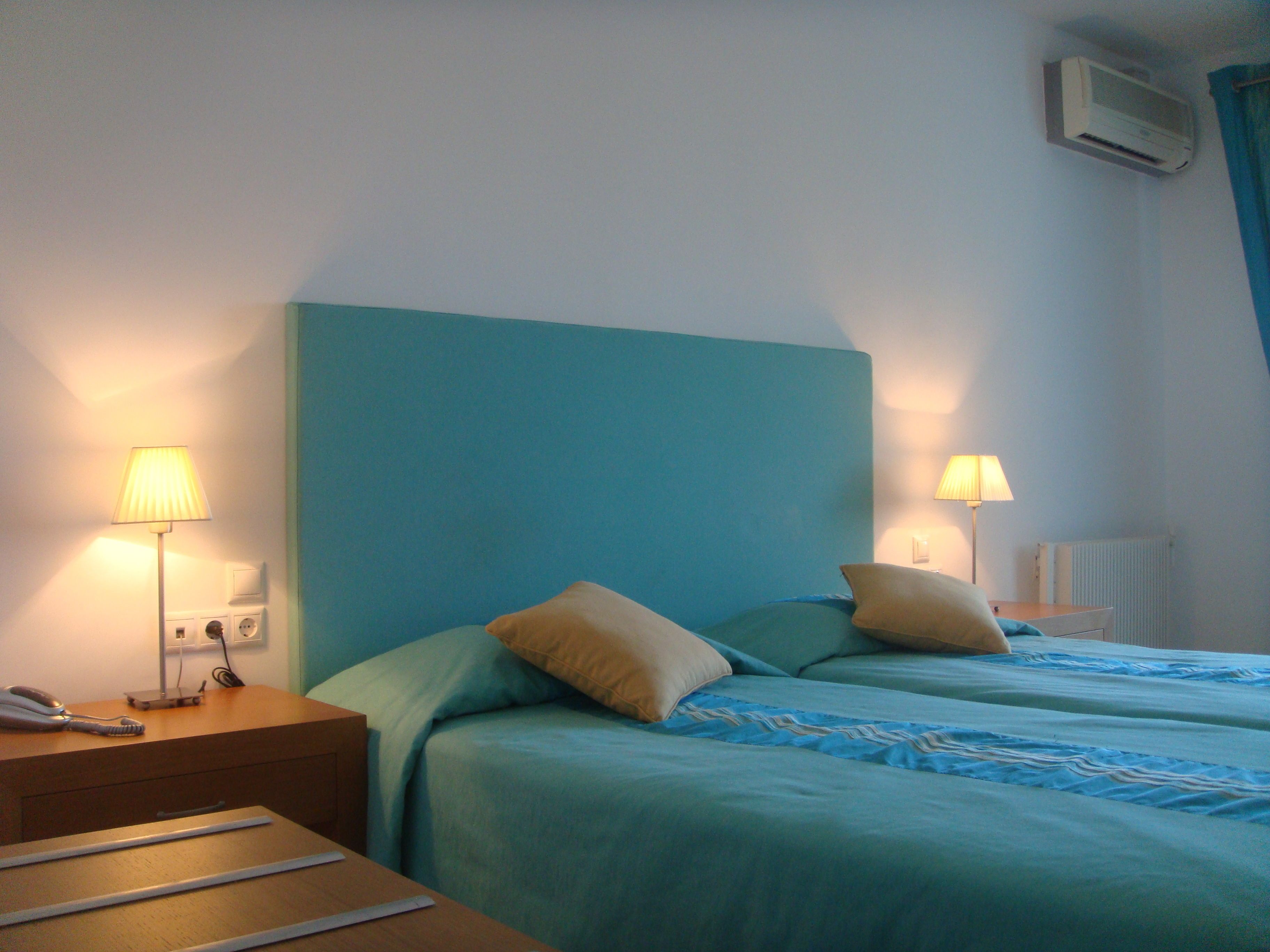 Una habitación de hotel con dos camas, una mesita de noche, una lámpara y un equipo de aire acondicionado.