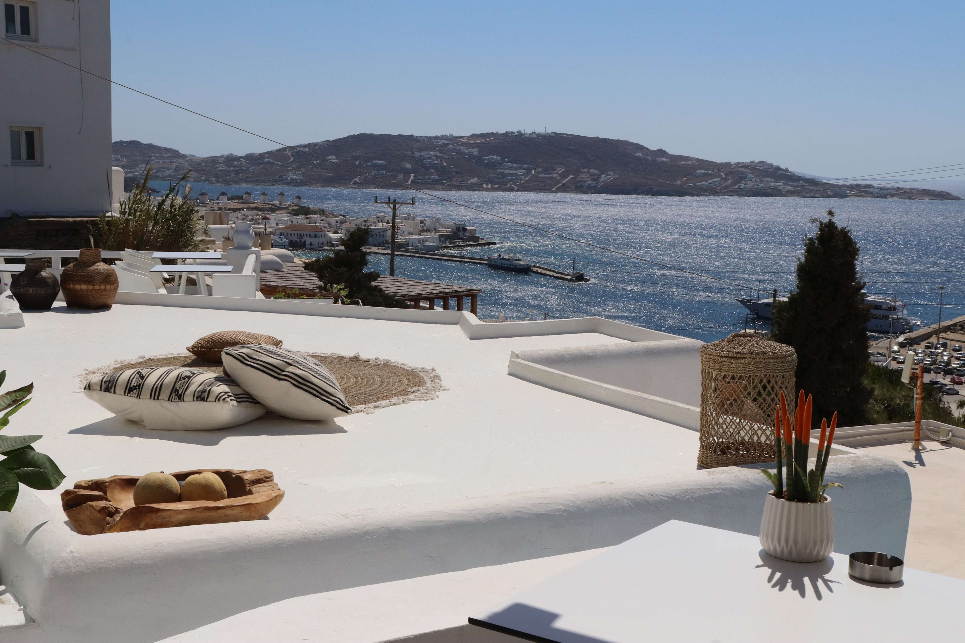 A terrace with white furniture, a view of the sea, and a mountain in the background.
