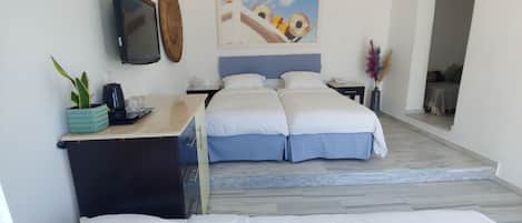 Una habitación de hotel con cama, escritorio con cafetera, televisor y un cuadro en la pared.