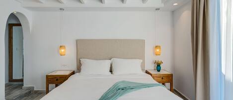 A hotel room with a large bed, two bedside tables, a headboard, and a window with curtains.