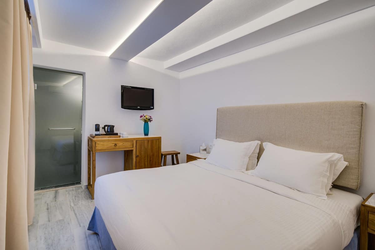 A hotel room with a bed, a desk, a TV, and a bathroom door.