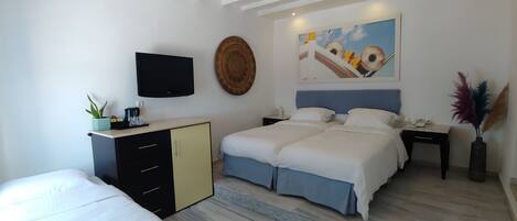 A bedroom with two beds, a TV, a painting, and a desk with a vase.