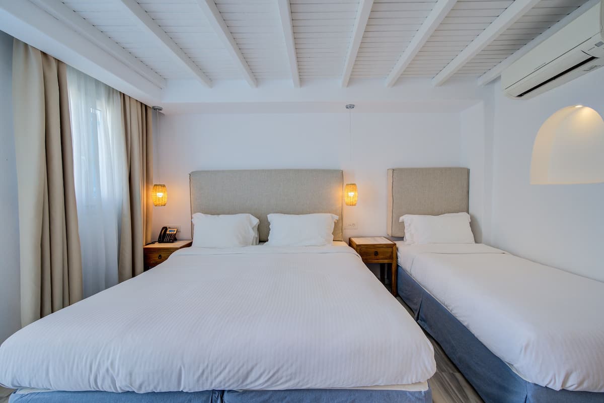 A hotel room with a large bed, two bedside tables, a nightstand, and a wall-mounted lamp.