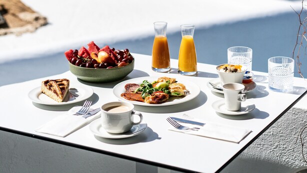 Una mesa con alimentos para el desayuno y dos vasos de jugo de naranja, con vistas a un paisaje costero.