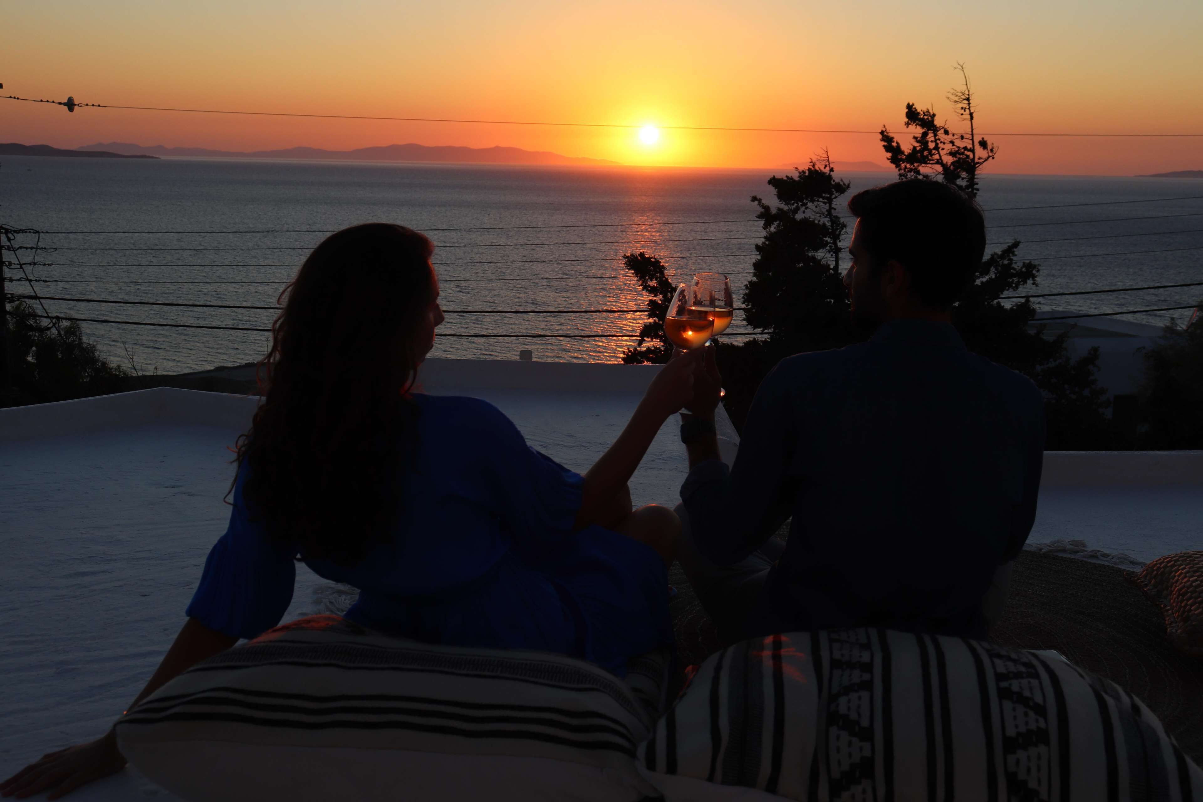 Two people sitting on a balcony overlooking a sunset over the sea.