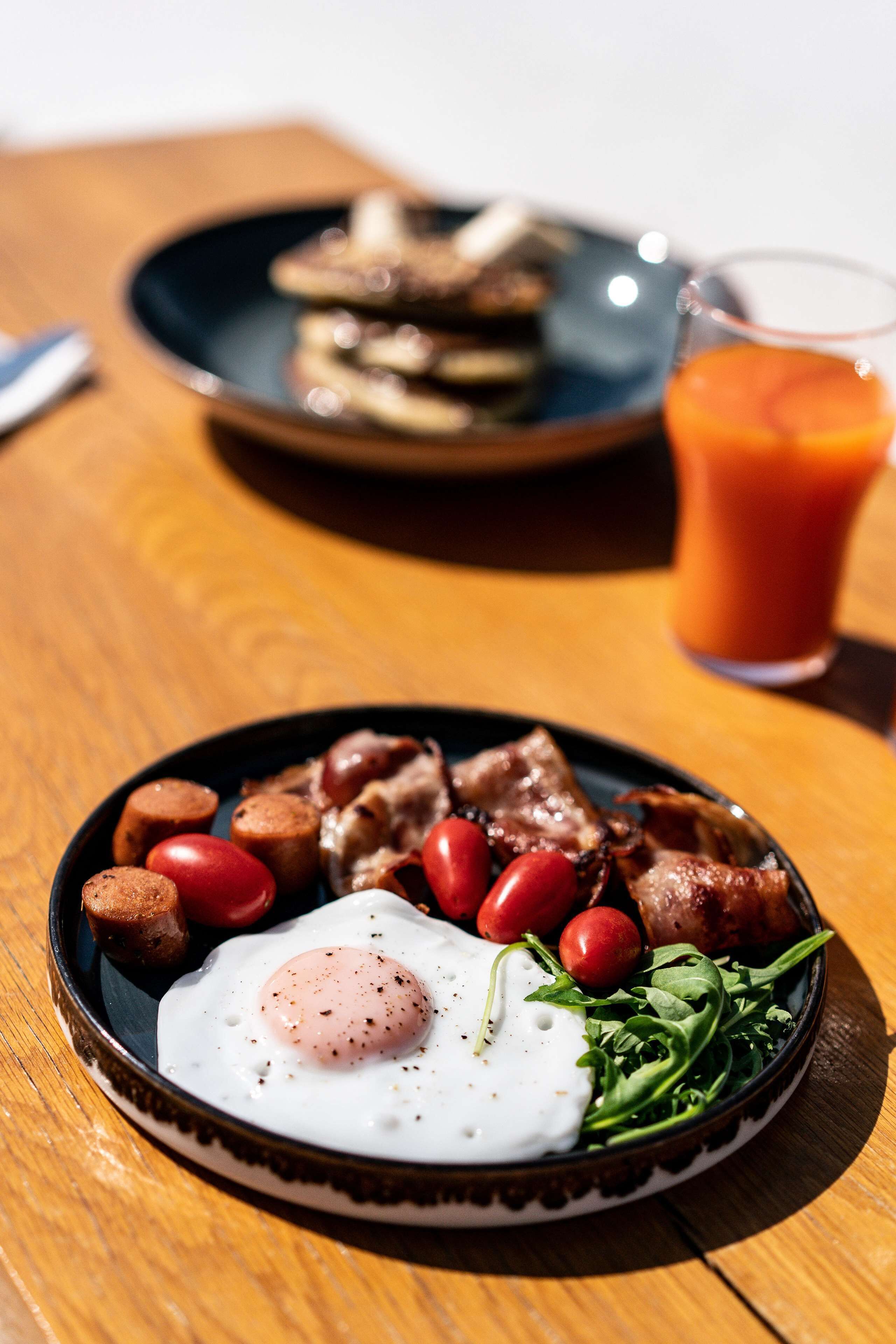 Un plato de desayuno con huevos, tomates, verduras de hoja y salchichas sobre una mesa de madera.