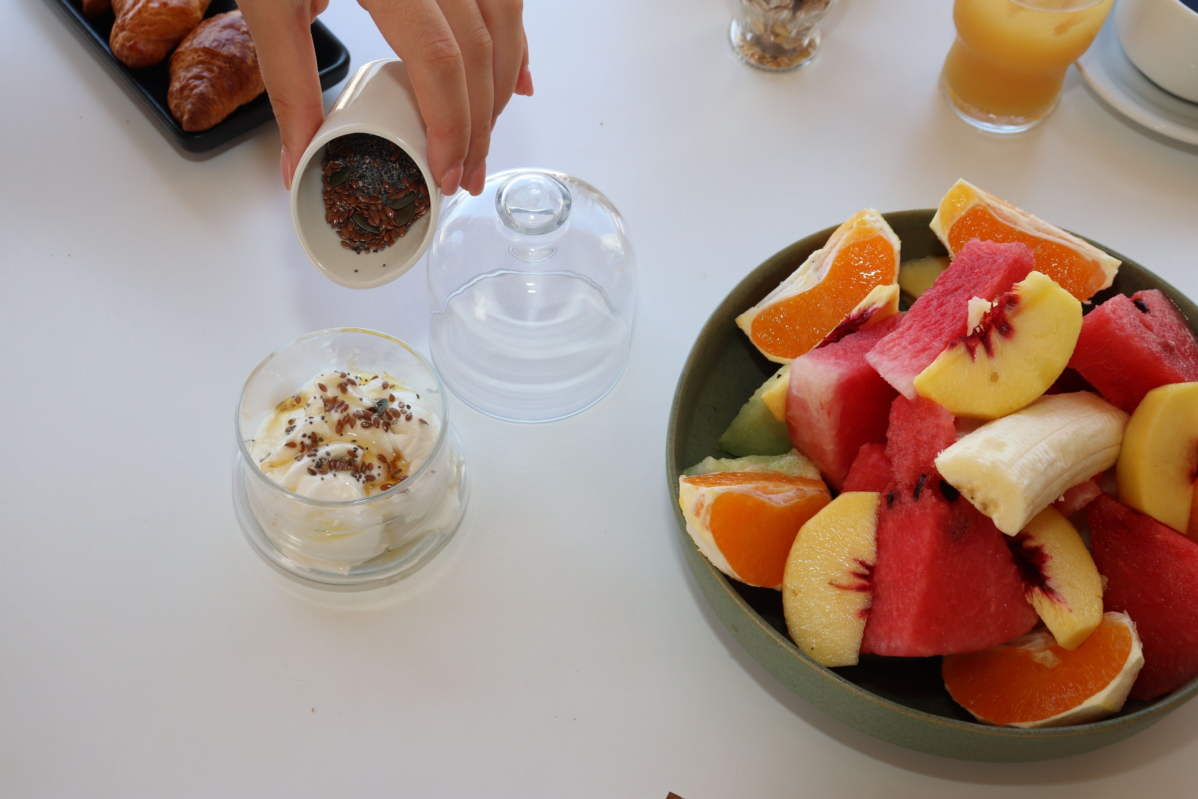 A breakfast setting with a bowl of fruit, a glass of juice, and a dessert with whipped cream and chocolate shavings.