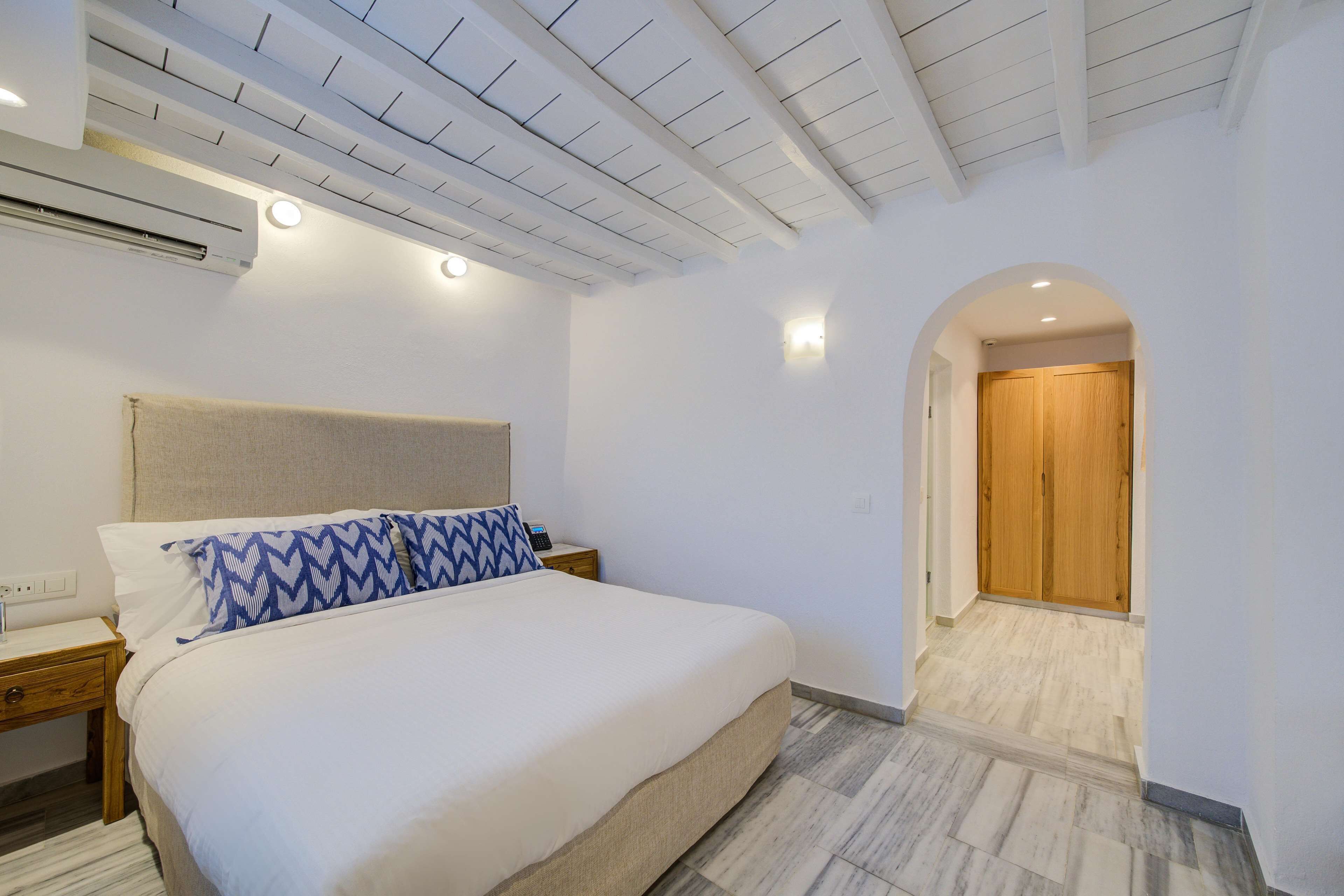 A bedroom with a bed, nightstands, an air conditioner, a wooden door, and a tiled floor.