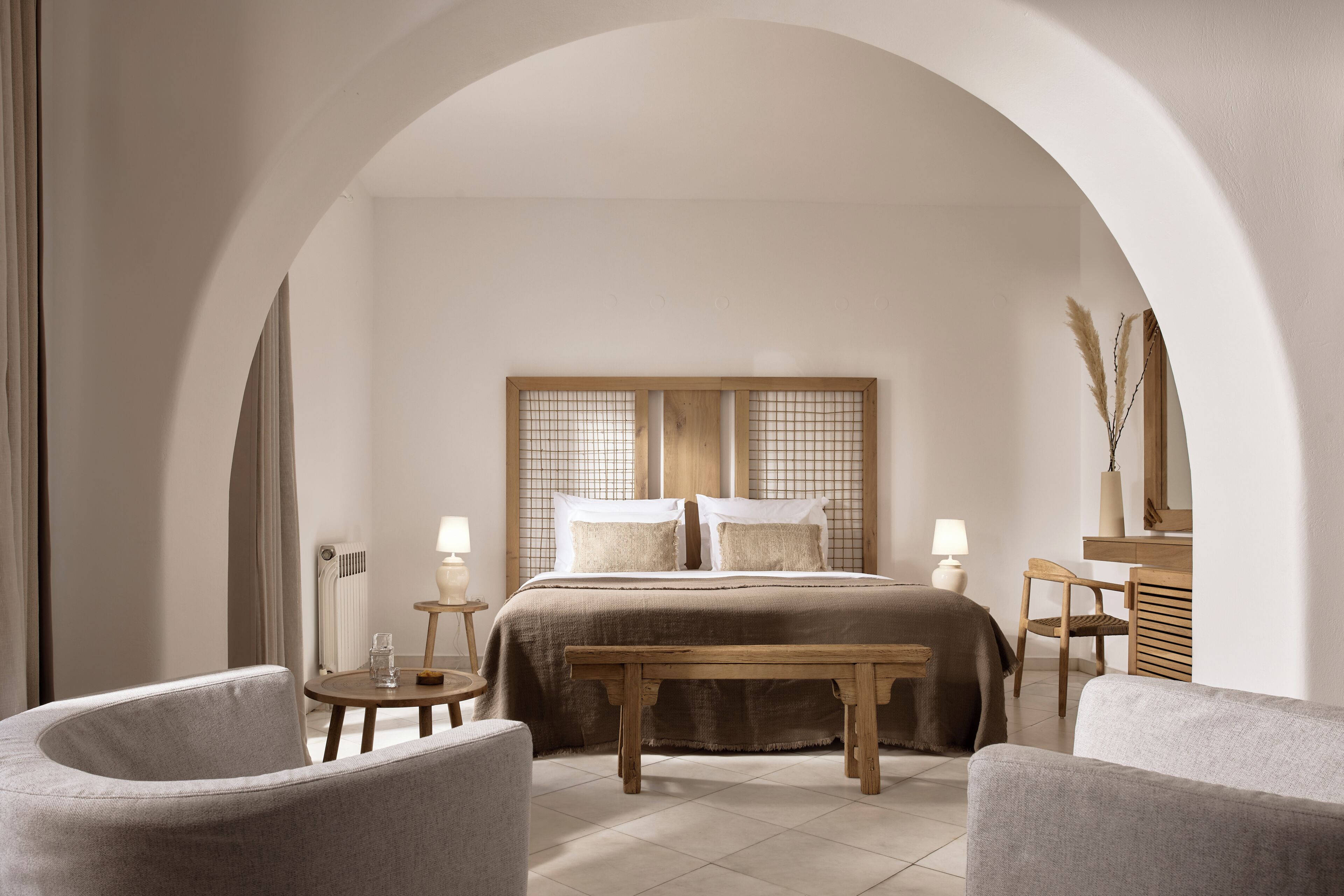 Ein Schlafzimmer mit einem Bett, zwei Nachttischen, einer Bank, einem Stuhl und einer gewölbten Tür.