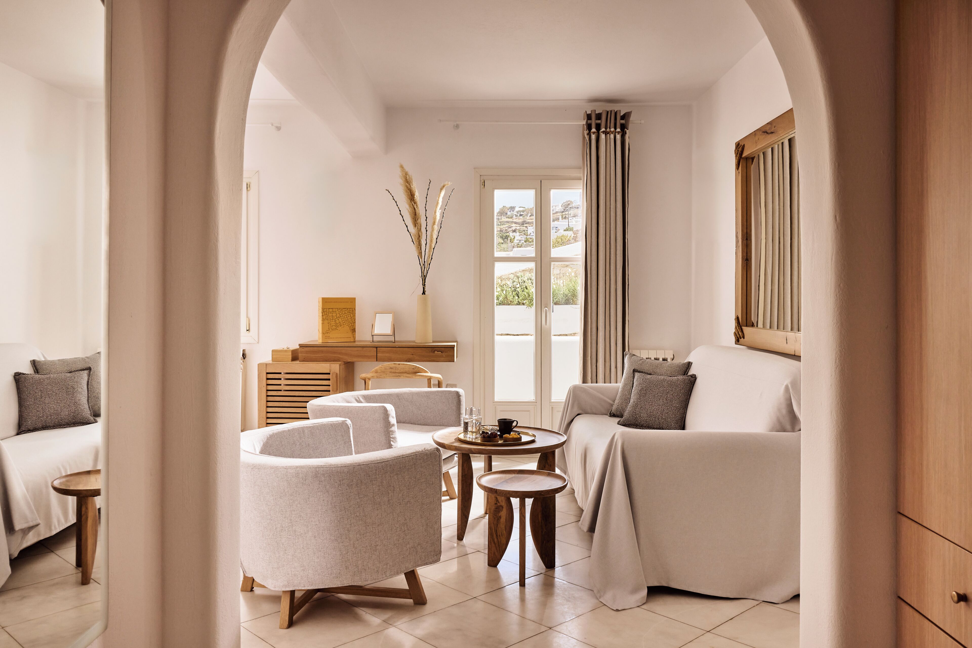 A modern living room with a sofa, armchair, and coffee table, a wooden cabinet, and a view through an archway.