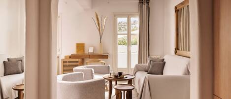 A modern living room with a sofa, armchair, and coffee table, a wooden cabinet, and a view through an archway.