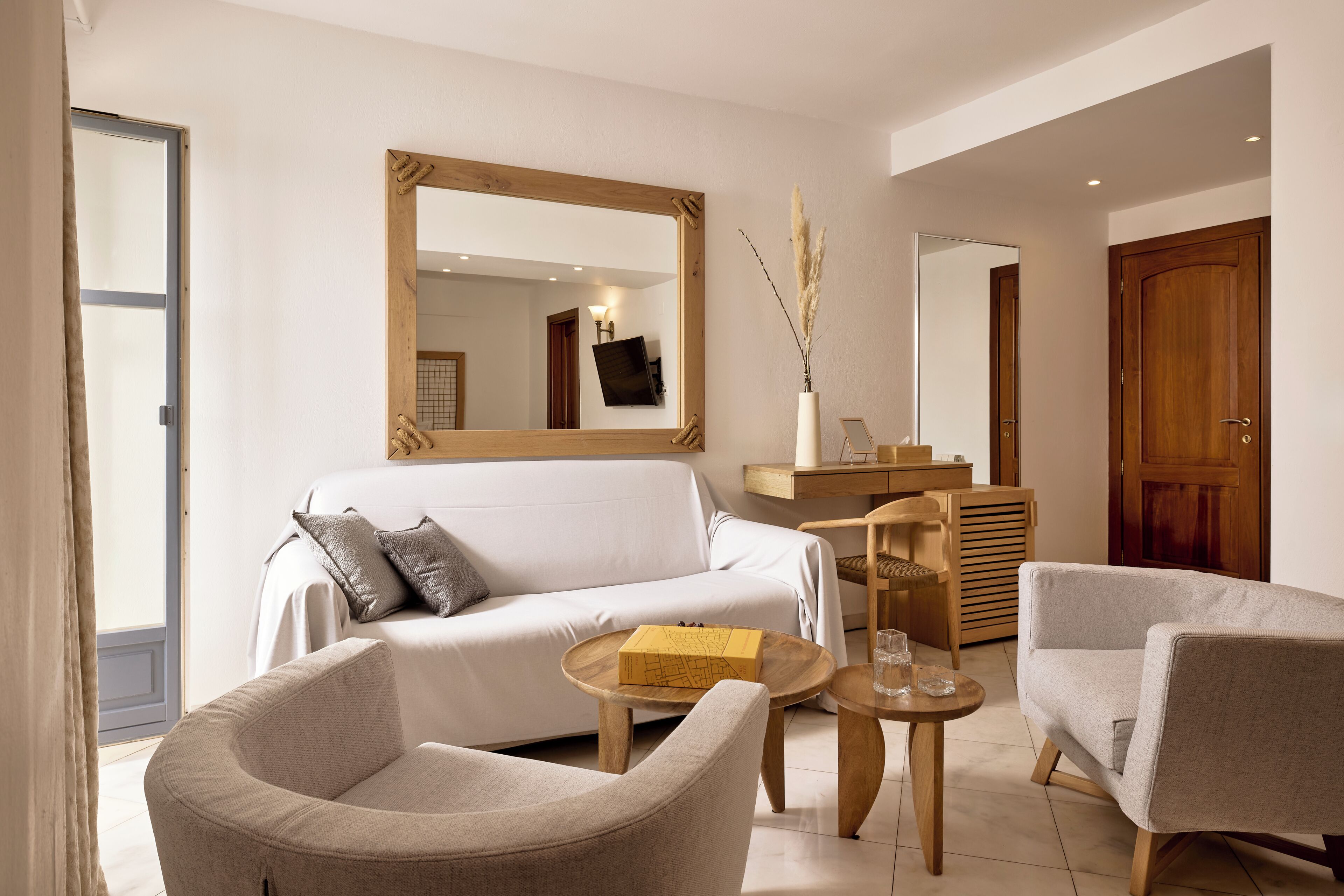 A modern living room with a white sofa, two armchairs, a wooden coffee table, and a large mirror.