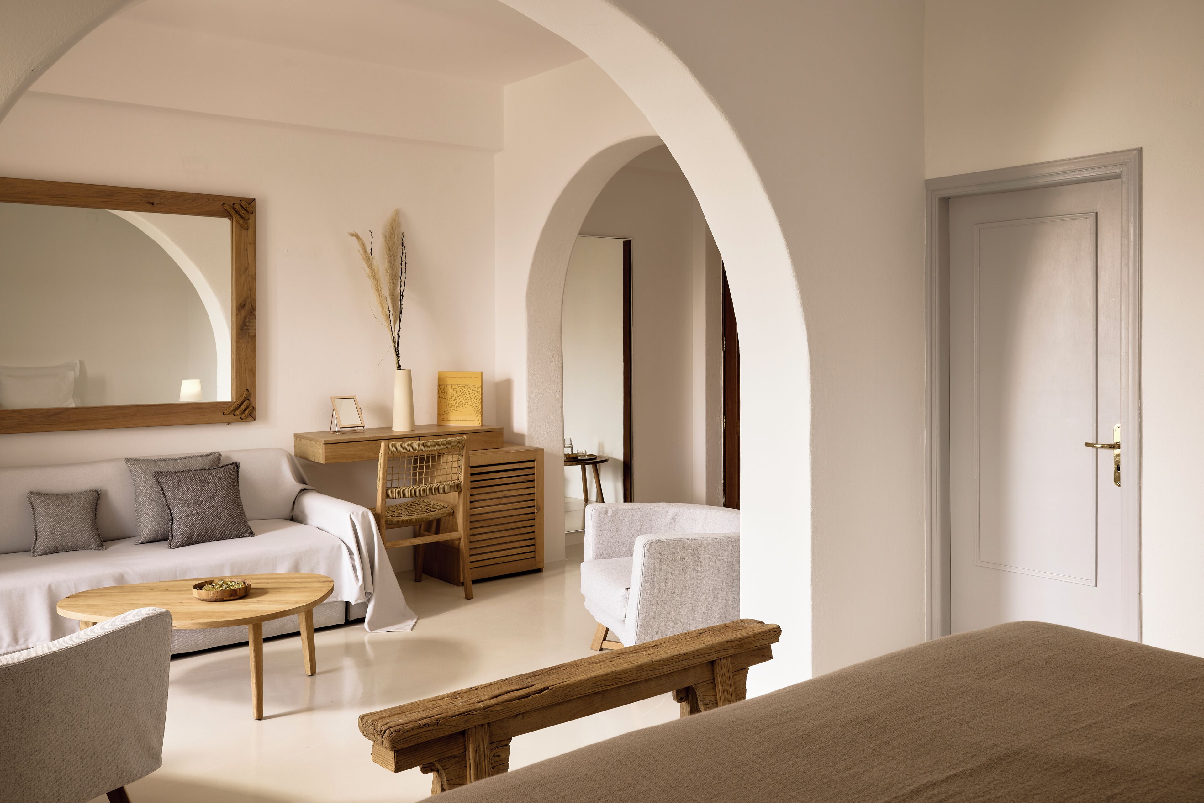 A room with a sofa, a wooden coffee table, a chair, a bed, and a door.